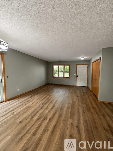 A room with wooden flooring and a window with a view of greenery outside.