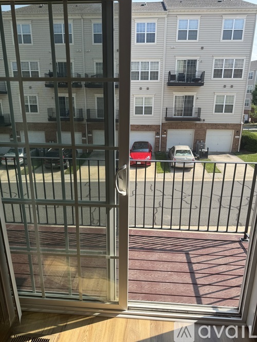 A view from a window looking out to a balcony with a red car and apartment buildings in the background.