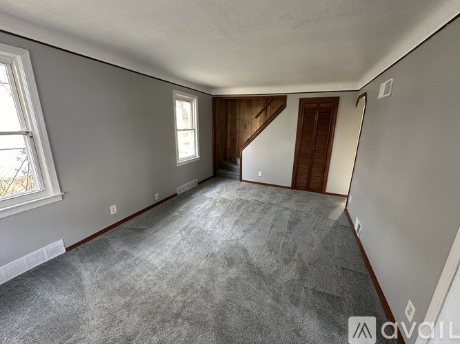 A spacious room with a carpeted floor and a staircase in the background.