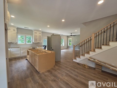 A spacious kitchen with wooden floors and a staircase with black railings.