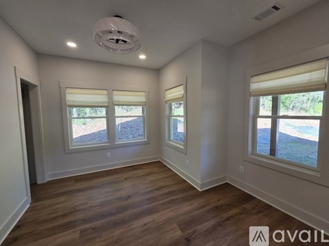 A room with wooden floors and two windows with blinds.