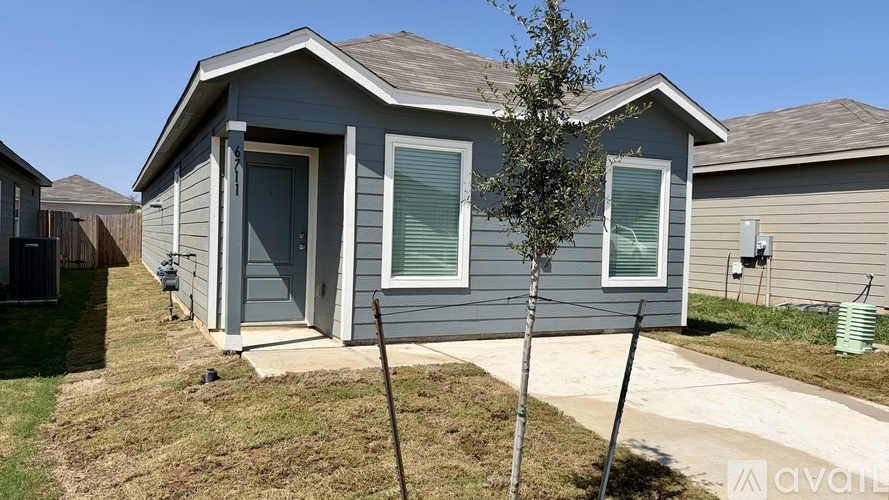 A small house with a grey front and a tree in front.