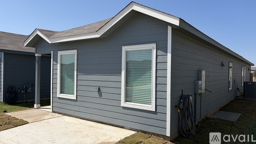 A grey house with a white window and a hose on the wall.