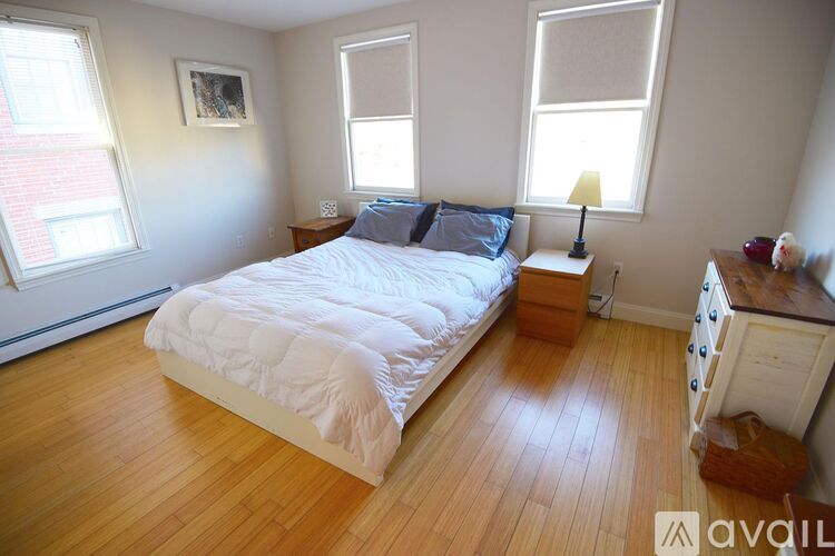 A bedroom with a large bed, wooden floors, and a window with blinds.