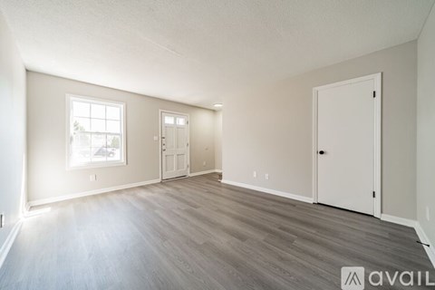 A spacious room with wooden flooring and white walls.