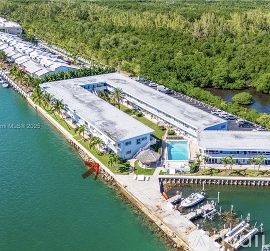 A large building with a pool is situated next to a body of water.