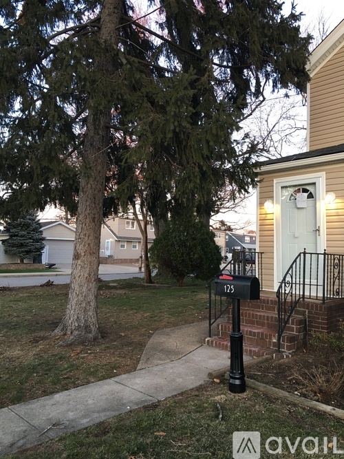 A tree stands in front of a house with a mailbox on a black pole.