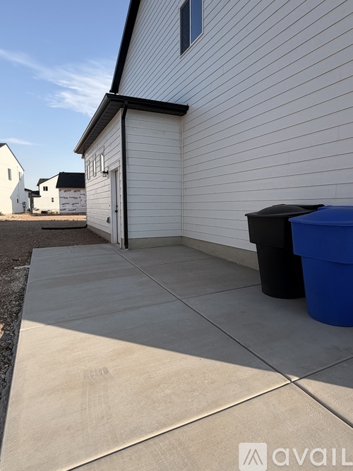 A white house with a black trash bin and a blue container on the concrete.