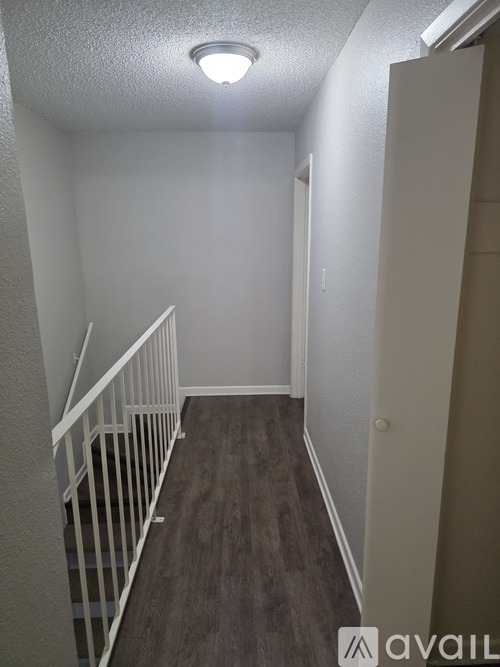 A hallway with a white railing and brown flooring.
