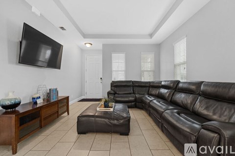 A living room with a black leather couch and a flat screen TV mounted on the wall.