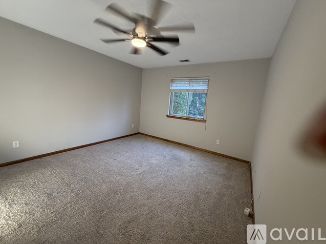 A room with a ceiling fan and a window with a view of trees.