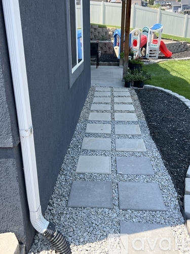 A concrete walkway with square tiles and a white pipe on the left.
