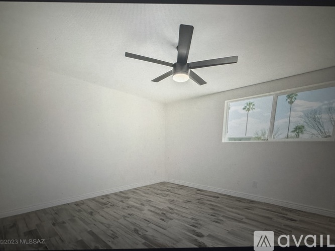 A room with a ceiling fan and a window showing a view of trees and a cloudy sky.