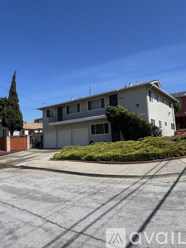 A white two-story house with a brown fence and a green tree in front.