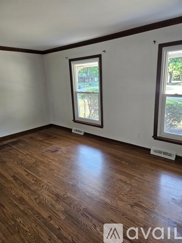 A room with wooden flooring and two windows.