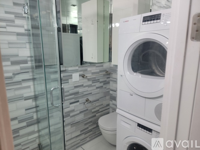 A white washing machine in a modern laundry room with a glass shower door.