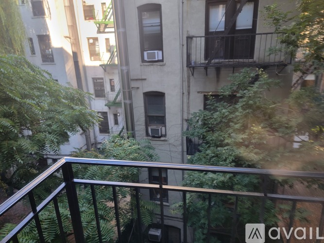 A balcony with a metal railing overlooks a courtyard with trees and buildings.