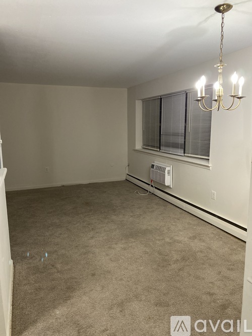 A room with a carpeted floor, a chandelier, and a window with blinds.