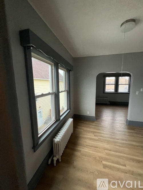 A room with wooden floors and a window with a view of a house across the street.