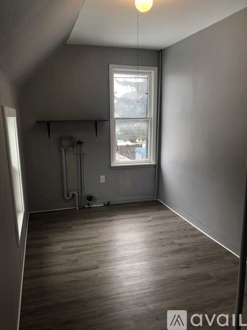 A room with wooden flooring and a window showing a view of a building outside.