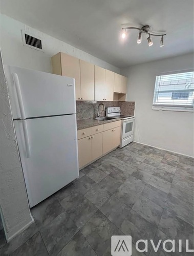 A kitchen with a white fridge, wooden cabinets, and a window.