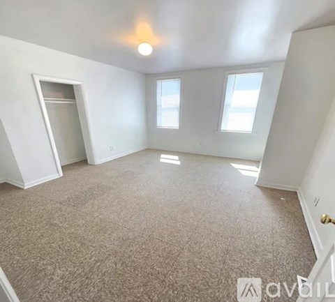 A spacious room with carpeted floor, two windows, and a door leading to another room.