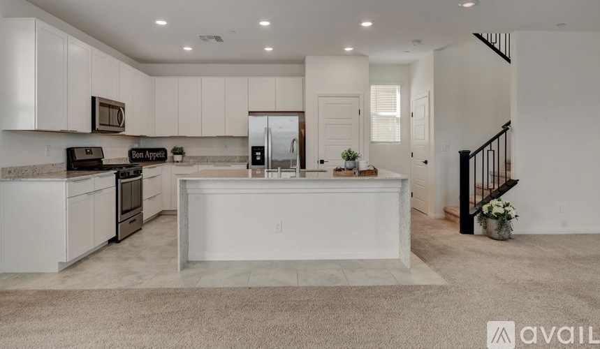 A modern kitchen with white cabinets and appliances, a large island in the center, and a staircase leading to the upper level.