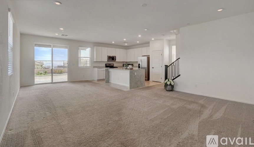 A spacious living room with a kitchen in the background and a carpet on the floor.