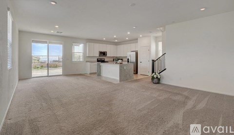 A spacious living room with a kitchen in the background and a carpet on the floor.