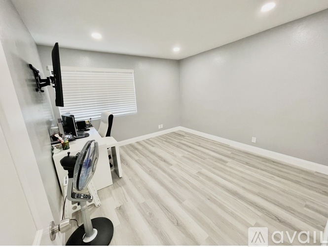 A room with a wooden floor and a fan on a stand.