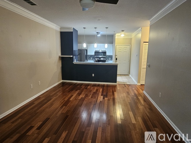 A room with wooden floors and a kitchen area in the background.