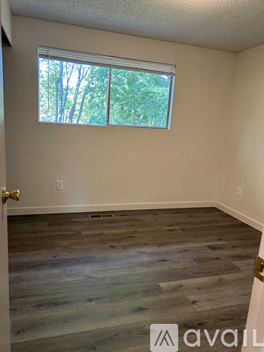 A room with wooden flooring and a window showing trees outside.