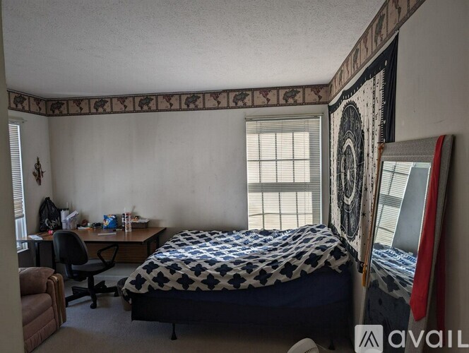A bedroom with a bed, desk, chair, and a surfboard leaning against the wall.