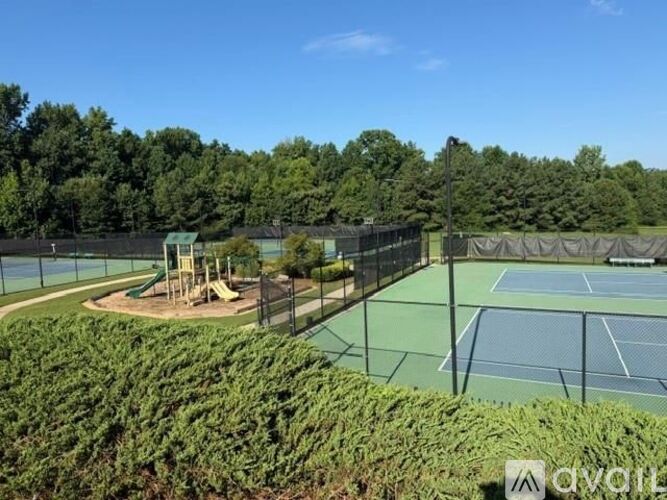 A tennis court surrounded by a green fence and trees.