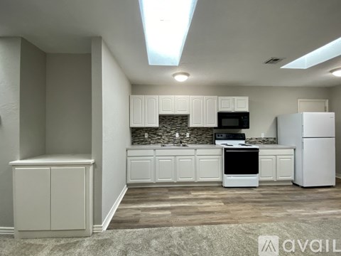 A kitchen with white cabinets and appliances, a stone backsplash, and a skylight.