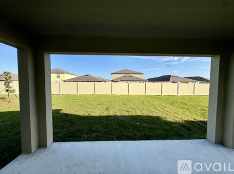 A view from a covered patio looking out to a grassy field and a row of houses.