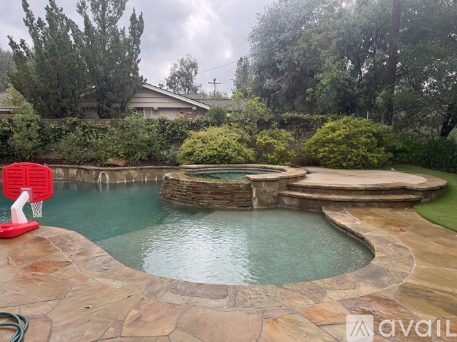 A red basketball hoop is in the foreground of a residential backyard with a small pool.