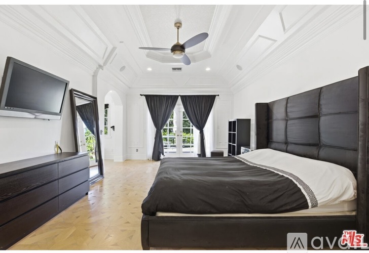 A bedroom with a large bed, a television, and a ceiling fan.