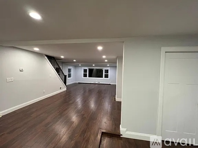 A spacious room with wooden floors and a staircase in the background.
