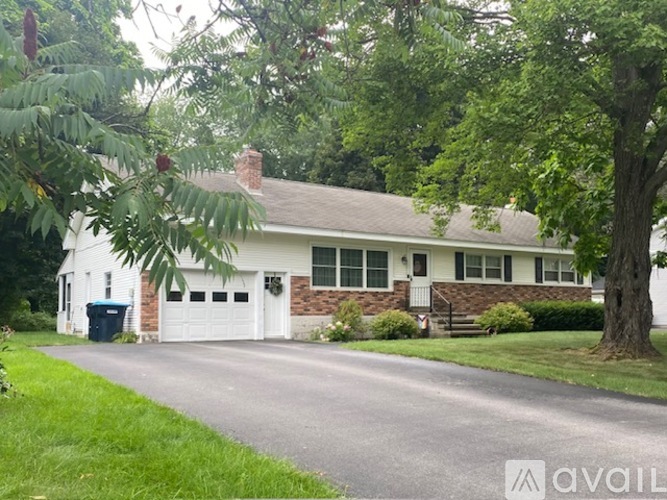 A white house with a brown roof and a tree in front.