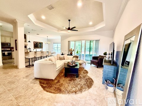 A spacious living room with a white sofa set, a brown rug, and a ceiling fan.