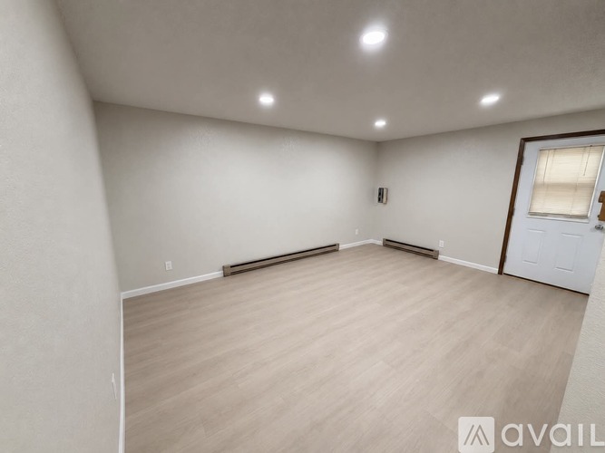 A spacious room with light wood flooring and white walls.