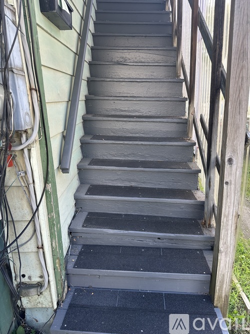A set of stairs with a wooden railing and a black mat on the bottom step.