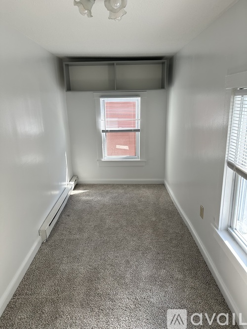A room with a carpeted floor, a window with blinds, and a wall-mounted air conditioner unit.