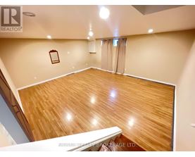 A spacious room with wooden flooring and a staircase on the left side.