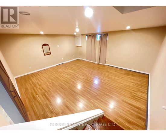 A spacious room with wooden flooring and a staircase on the left side.