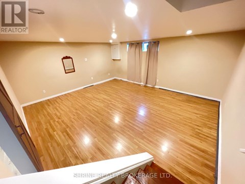 A spacious room with wooden flooring and a staircase on the left side.