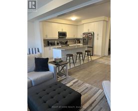 A modern kitchen with a bar stool and a black ottoman.