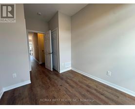 A room with wood flooring and white walls, with a doorway leading to another room.