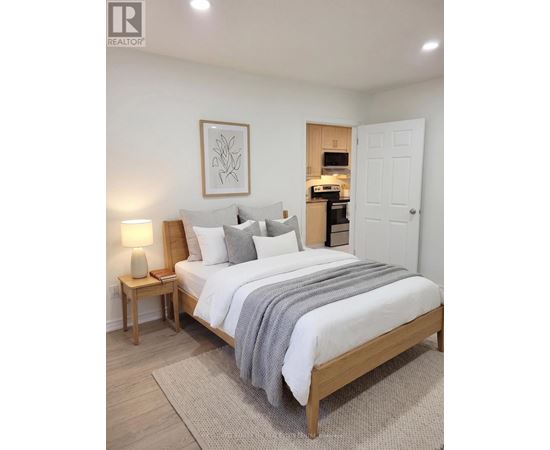 A bedroom with a large bed, a nightstand with a lamp, and a framed picture on the wall.
